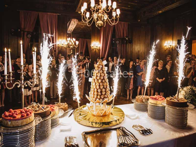 Buffet de desserts avec pièce montée et cierges magiques, dans une salle élégante avec invités en arrière-plan.