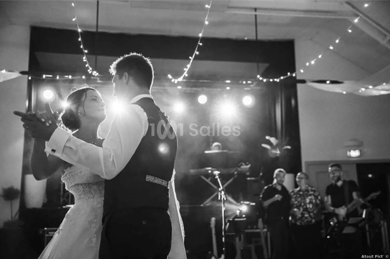 Un couple danse sous des lumières tamisées lors d'une réception, avec un groupe jouant en arrière-plan.