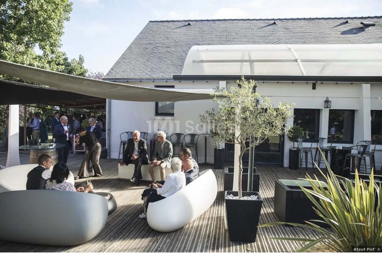 Personnes assises et debout sur une terrasse en bois, entourées de mobilier moderne et de végétation.