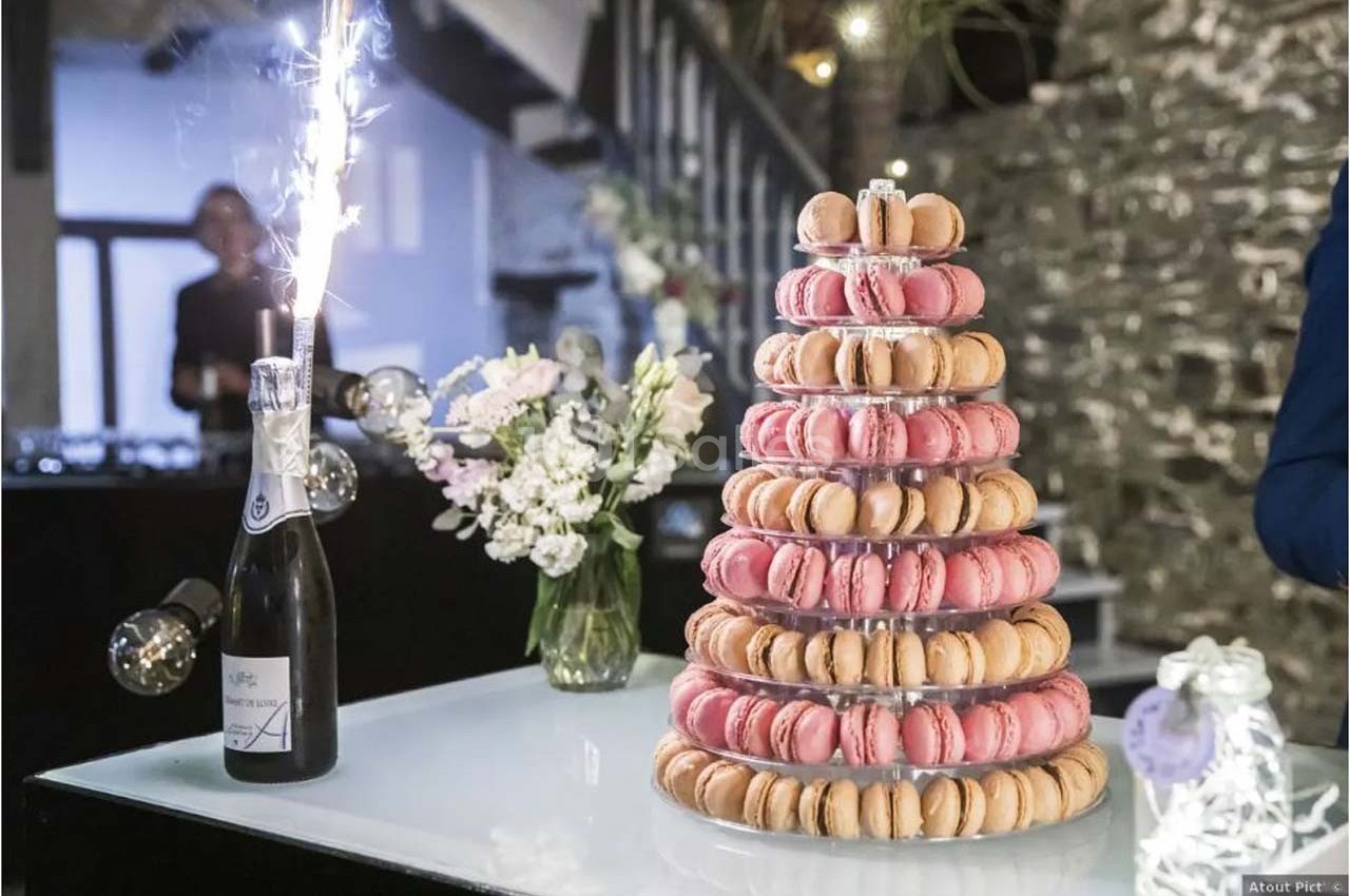 Tour de macarons colorés sur une table avec une bouteille de champagne et un bouquet de fleurs en arrière-plan.