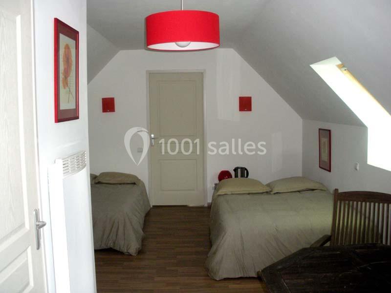 Chambre mansardée avec deux lits simples, parquet au sol, murs blancs et décorations rouges.