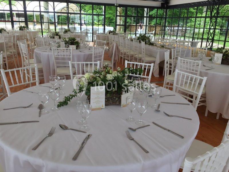 Salle de réception lumineuse avec tables rondes dressées, nappes blanches et décorations florales élégantes.