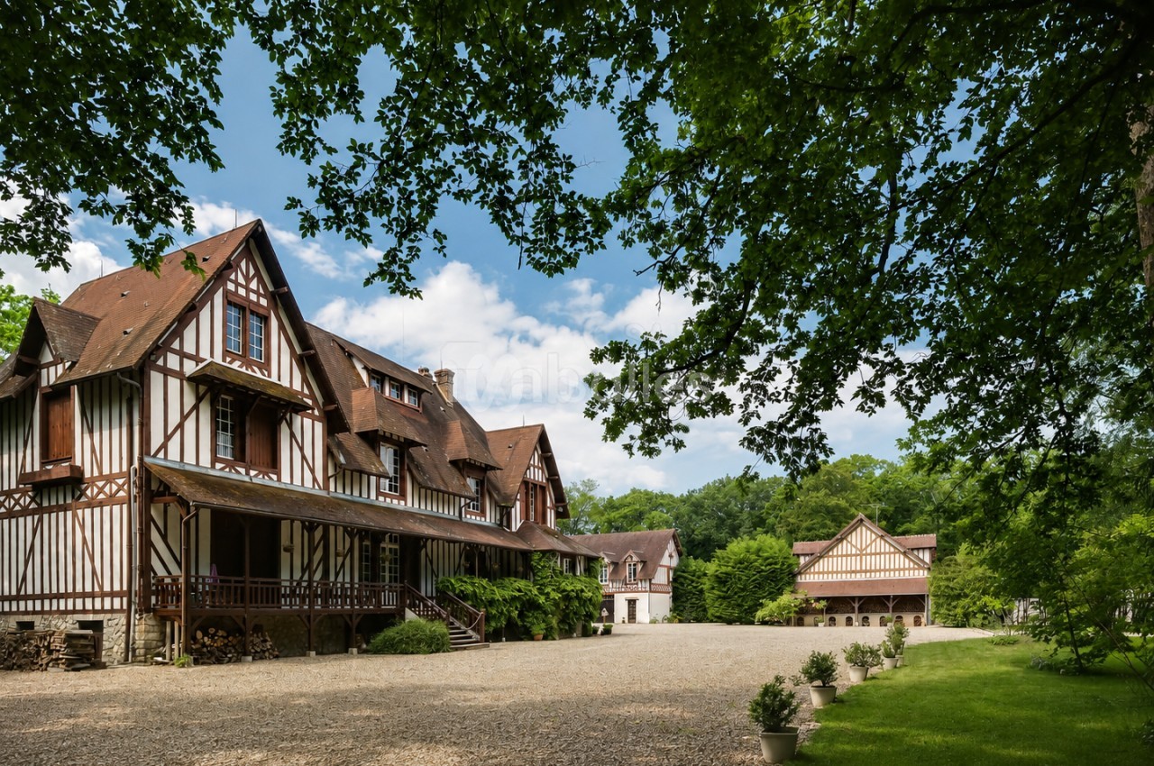 Grand bâtiment à colombages entouré d'arbres, avec une cour en gravier et un jardin verdoyant.