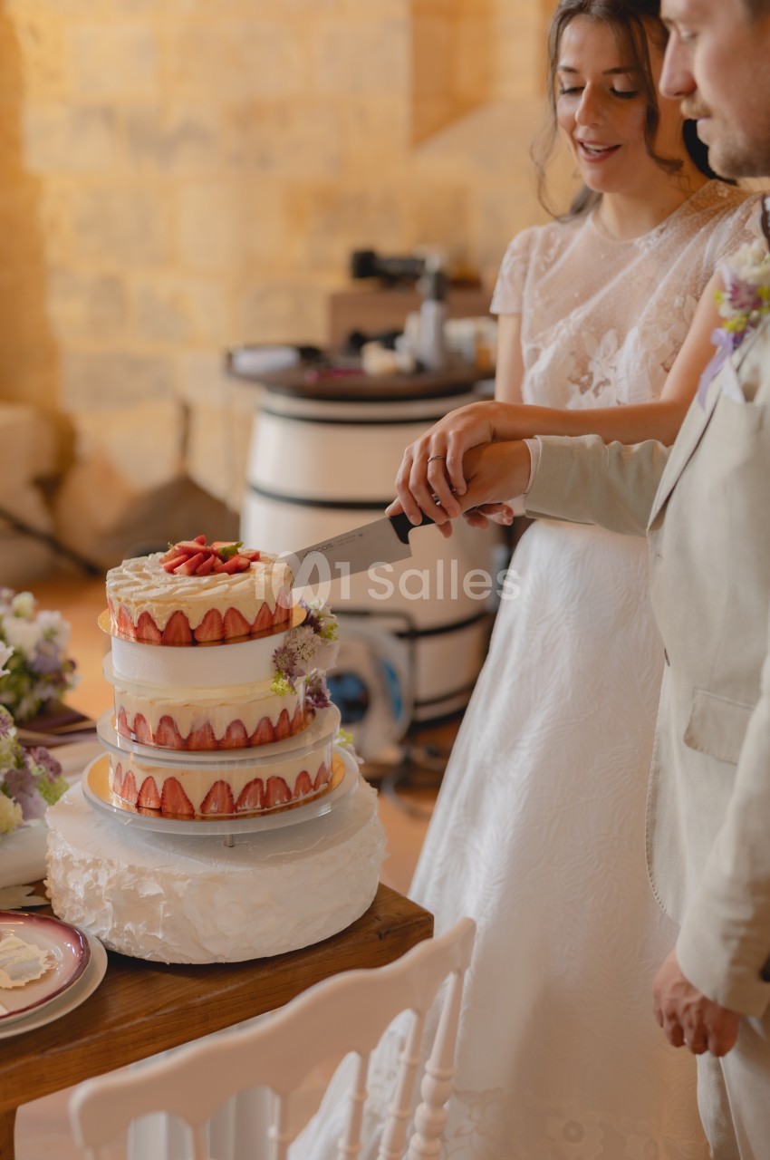 Un couple en tenue de mariage coupe ensemble un gâteau à étages décoré de fraises et de fleurs.
