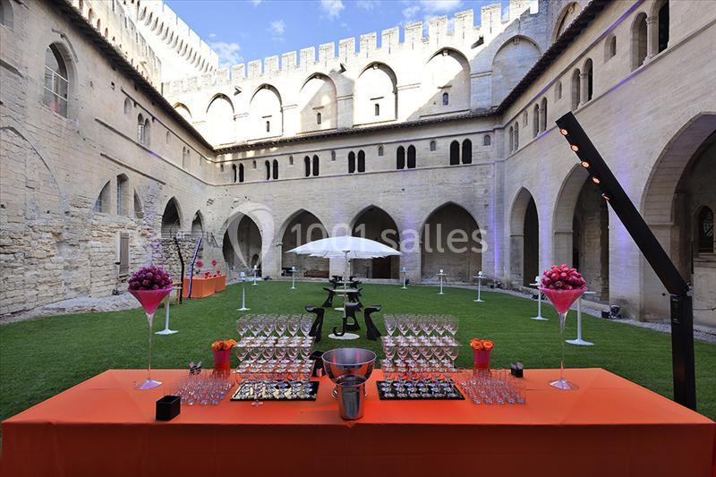 Table dressée avec verres et décorations colorées dans une cour intérieure historique avec pelouse et parasol blanc.