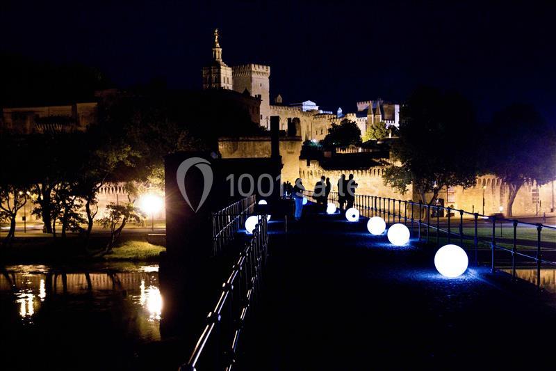 Passerelle illuminée par des sphères lumineuses menant à un bâtiment historique éclairé de nuit.