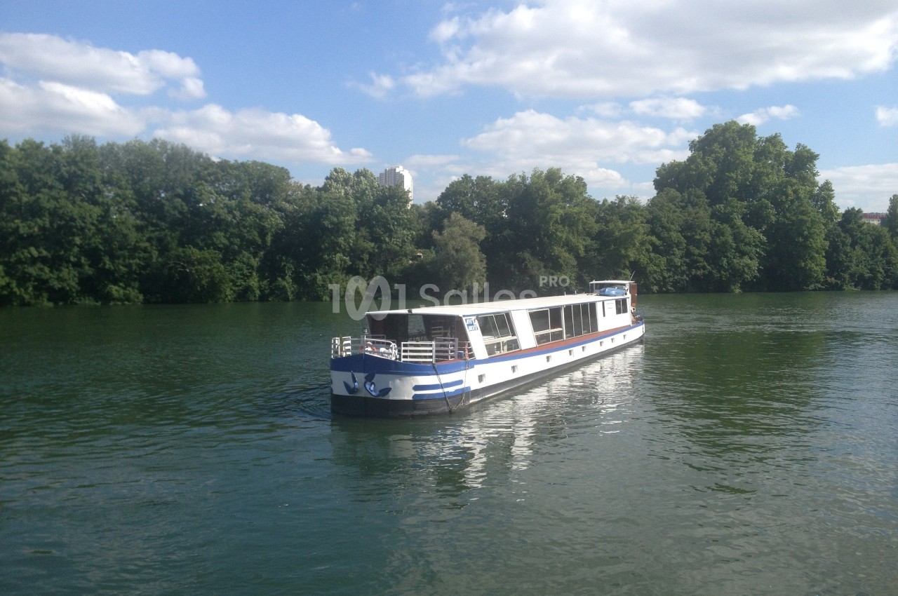 Bateau de plaisance blanc et bleu naviguant sur une rivière entourée de végétation et d'arbres.