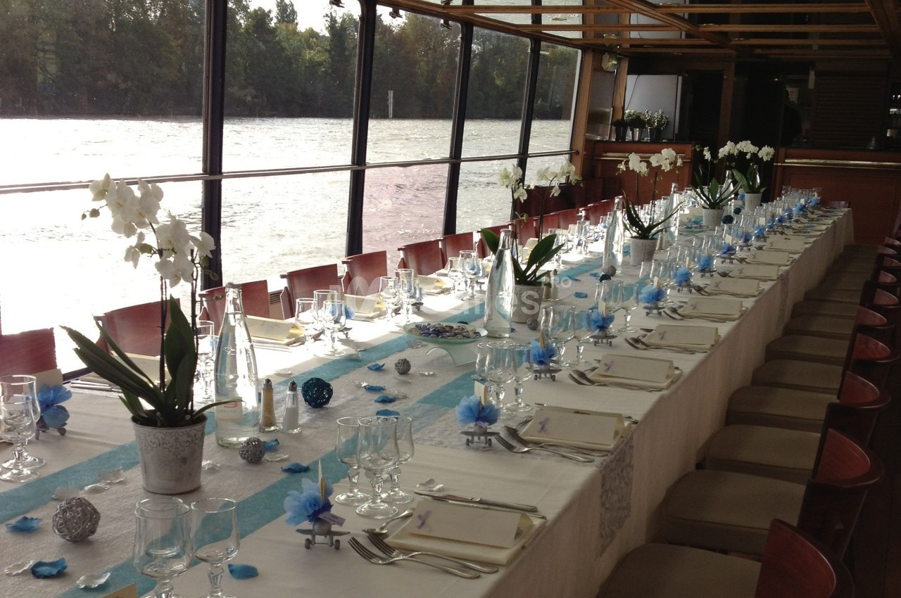 Table élégamment dressée avec nappes blanches, décorations bleues et blanches, et orchidées en centre de table.