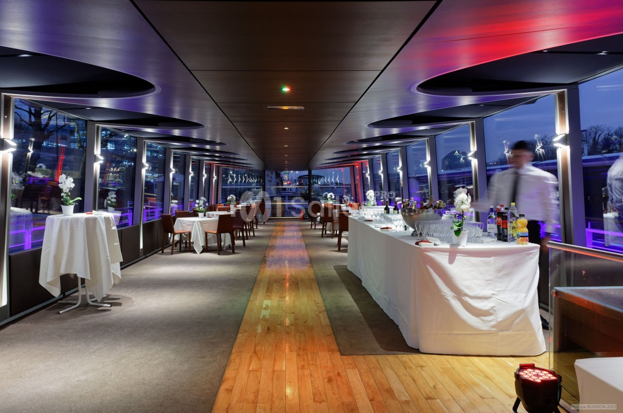 Salle de réception moderne avec tables dressées, buffet et grandes baies vitrées donnant sur un paysage nocturne.