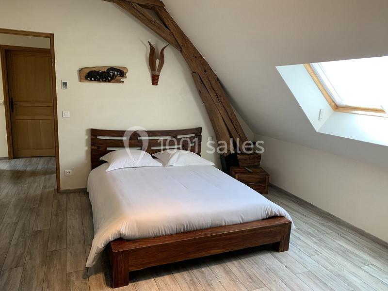 Lit double avec draps blancs dans une chambre mansardée, parquet au sol et poutres apparentes.