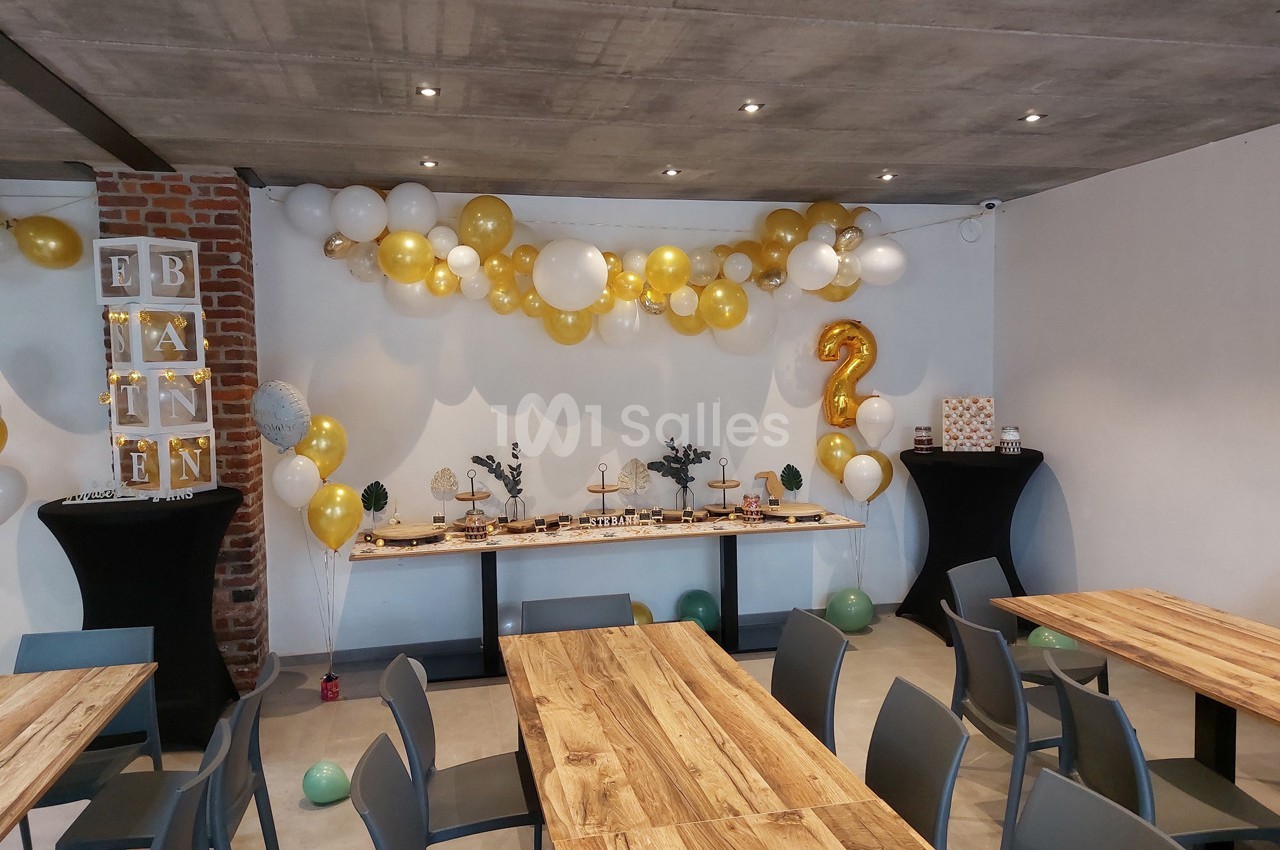 Salle décorée pour une fête avec des ballons blancs et dorés, une table de buffet et un chiffre 2 en ballon doré.