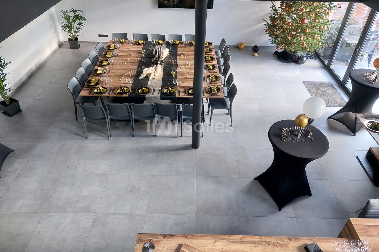 Salle moderne avec une grande table dressée pour un repas, décorée de tons dorés, et un sapin de Noël en arrière-plan.