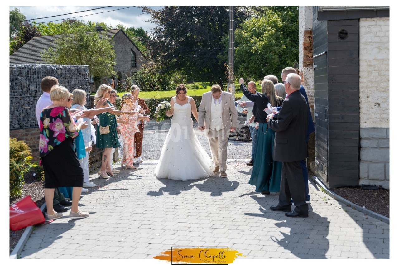 Un couple de mariés marche main dans la main sous les applaudissements des invités dans une allée extérieure.