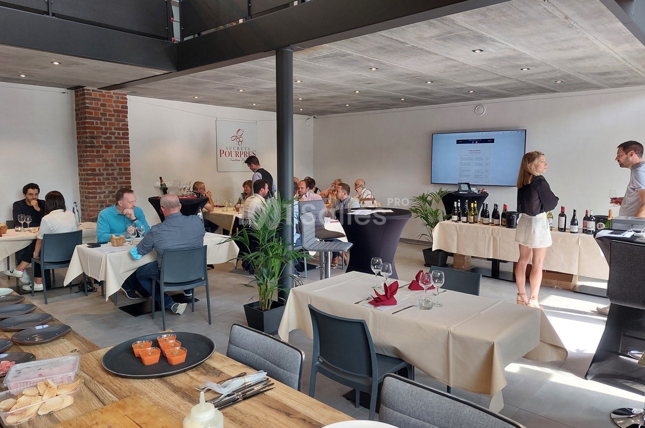 Des personnes dînent et discutent dans un restaurant lumineux avec des tables dressées et des bouteilles exposées.