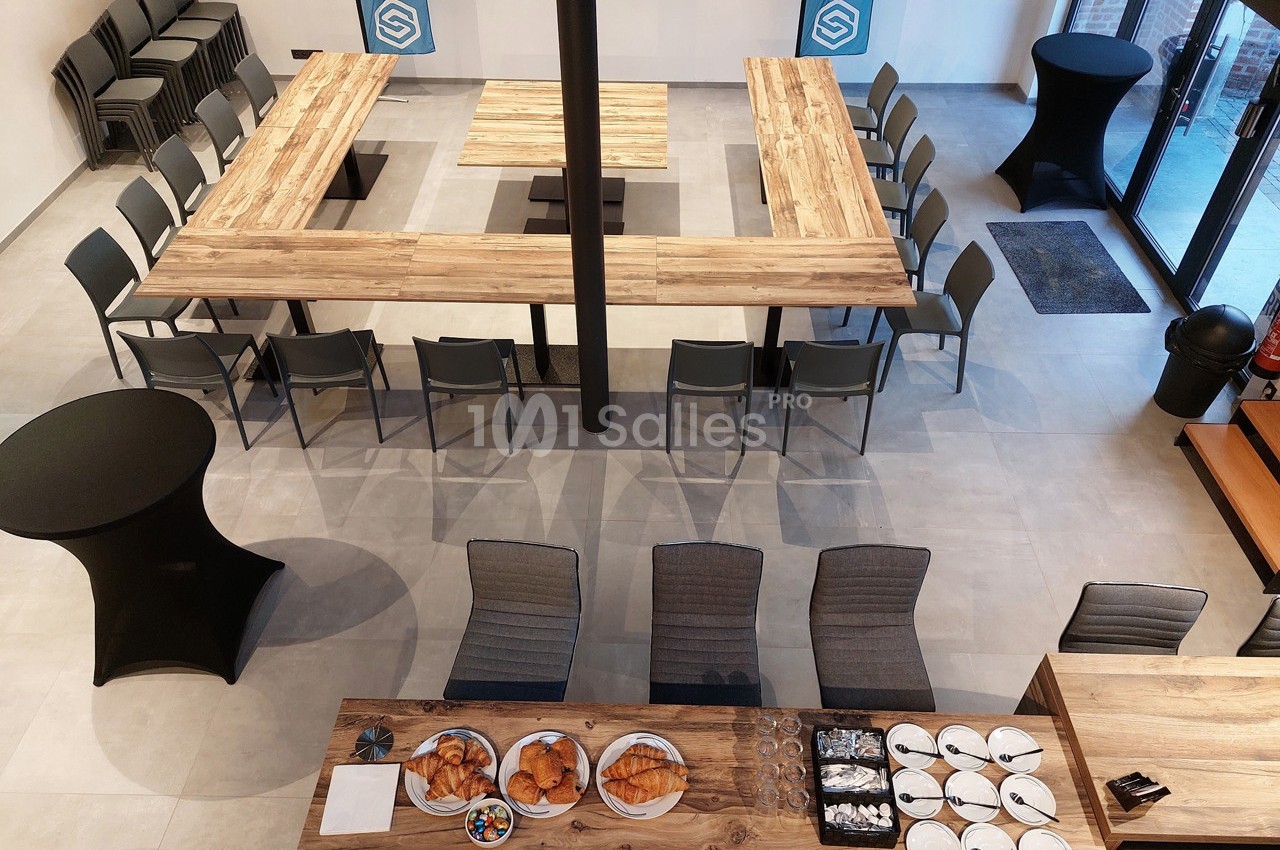 Salle de réunion aménagée en U avec des chaises, tables en bois, et buffet de viennoiseries au premier plan.
