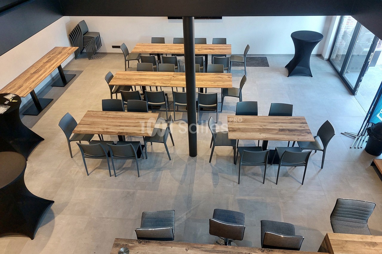 Salle moderne avec tables en bois, chaises grises et lumière naturelle entrant par de grandes baies vitrées.