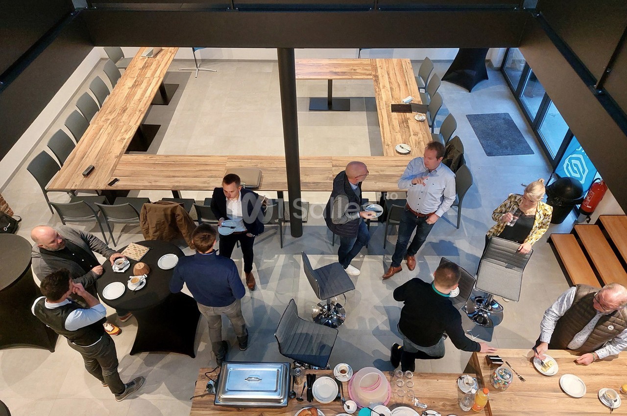 Personnes debout dans une salle de réunion, discutant et partageant un buffet autour de tables en bois disposées en U.