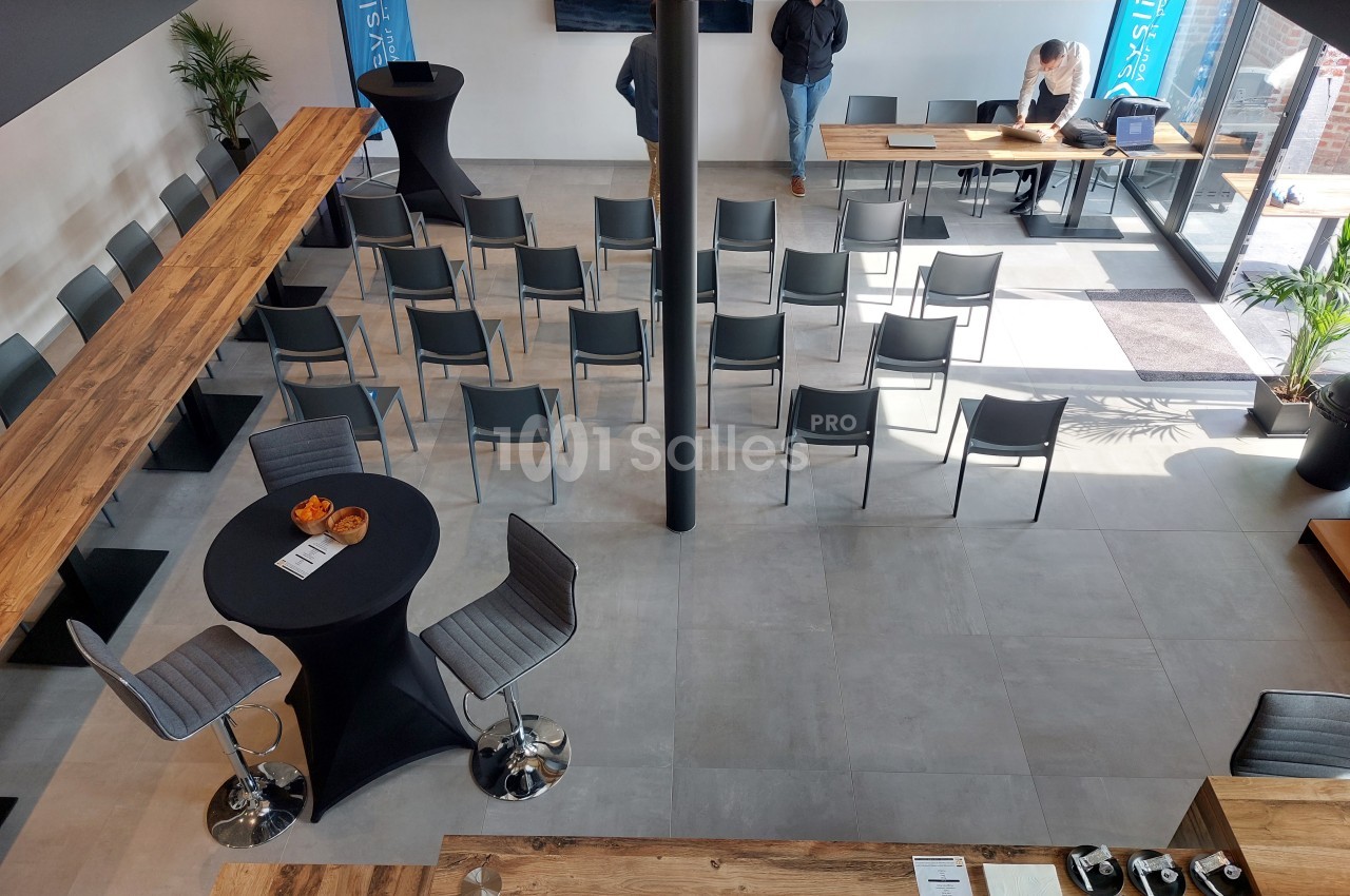 Salle de réunion moderne avec chaises disposées en rangées, tables hautes et grandes baies vitrées laissant entrer la…