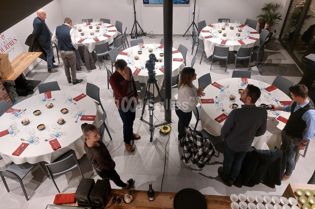 Salle aménagée avec des tables rondes dressées, des personnes discutent près d'un équipement de caméra.