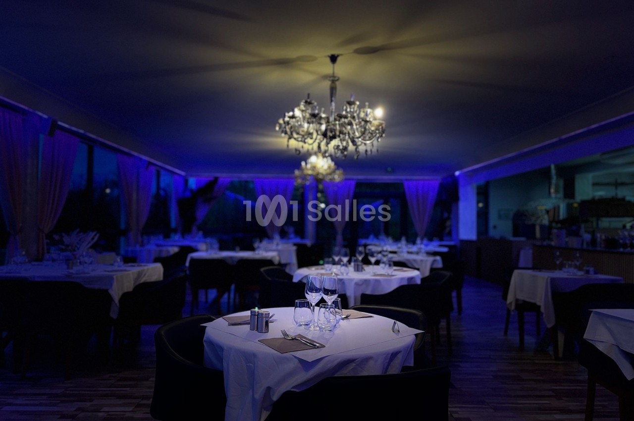 Salle de restaurant élégante éclairée par des lustres, avec tables dressées et ambiance tamisée.