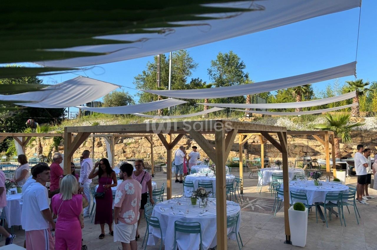 Personnes réunies dans un espace extérieur décoré avec des tables dressées et des voilages suspendus.