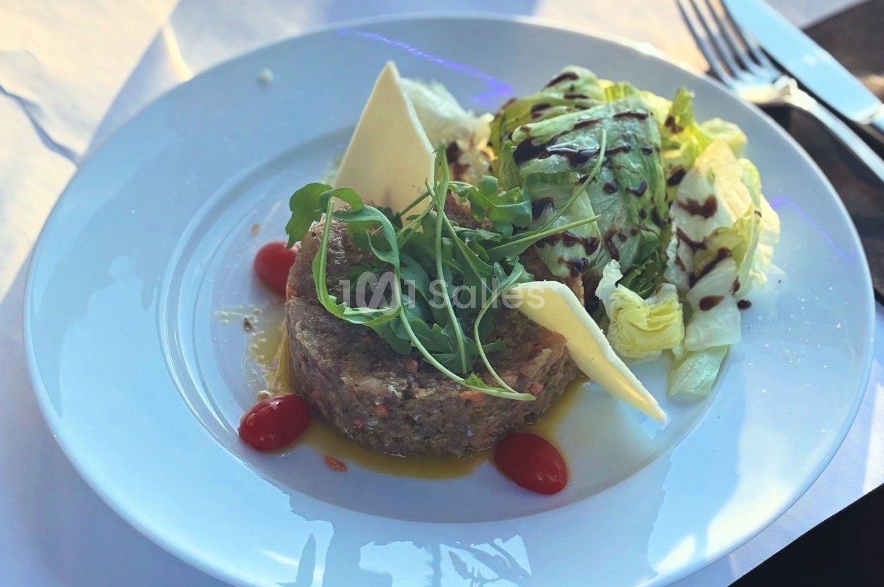 Assiette composée de tartare de viande, roquette, tomates cerises, copeaux de fromage et salade avec sauce balsamique.
