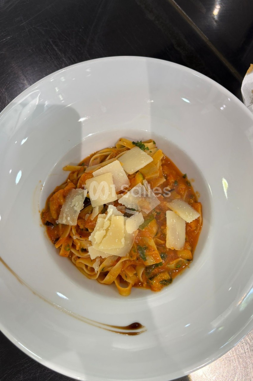 Assiette de tagliatelles à la sauce tomate, garnies de copeaux de parmesan et de persil, servie dans un bol blanc.