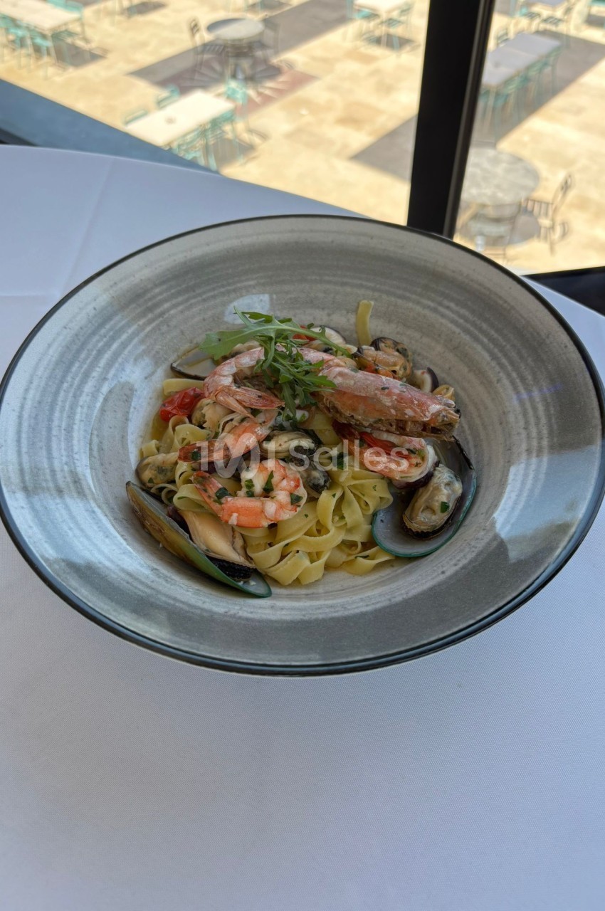 Assiette de tagliatelles aux fruits de mer avec crevettes, moules et sauce crémeuse, servie sur une nappe blanche.