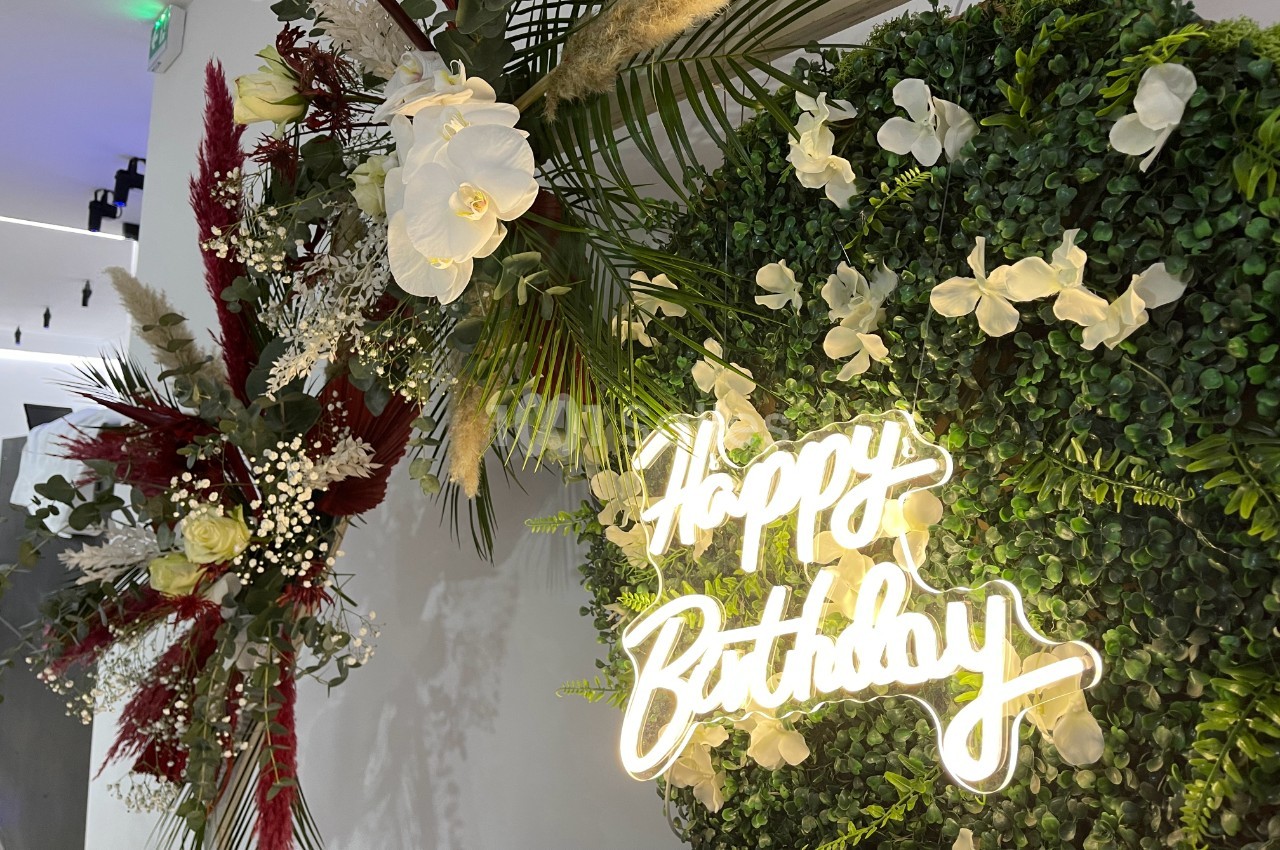 Mur végétal décoré de fleurs blanches et rouges avec une enseigne lumineuse ’Happy Birthday’.