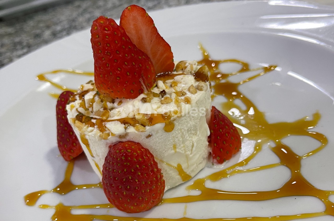 Dessert glacé garni de fraises fraîches, de morceaux de noix et de caramel, présenté sur une assiette blanche.