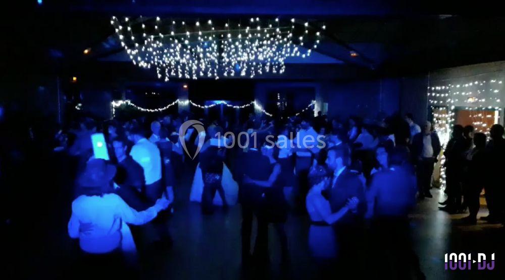 Salle sombre avec des guirlandes lumineuses au plafond, des personnes dansant et discutant lors d'un événement festif.