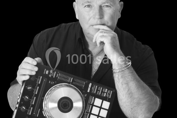 Homme tenant une console de mixage DJ, posé devant un fond noir, avec une expression réfléchie.