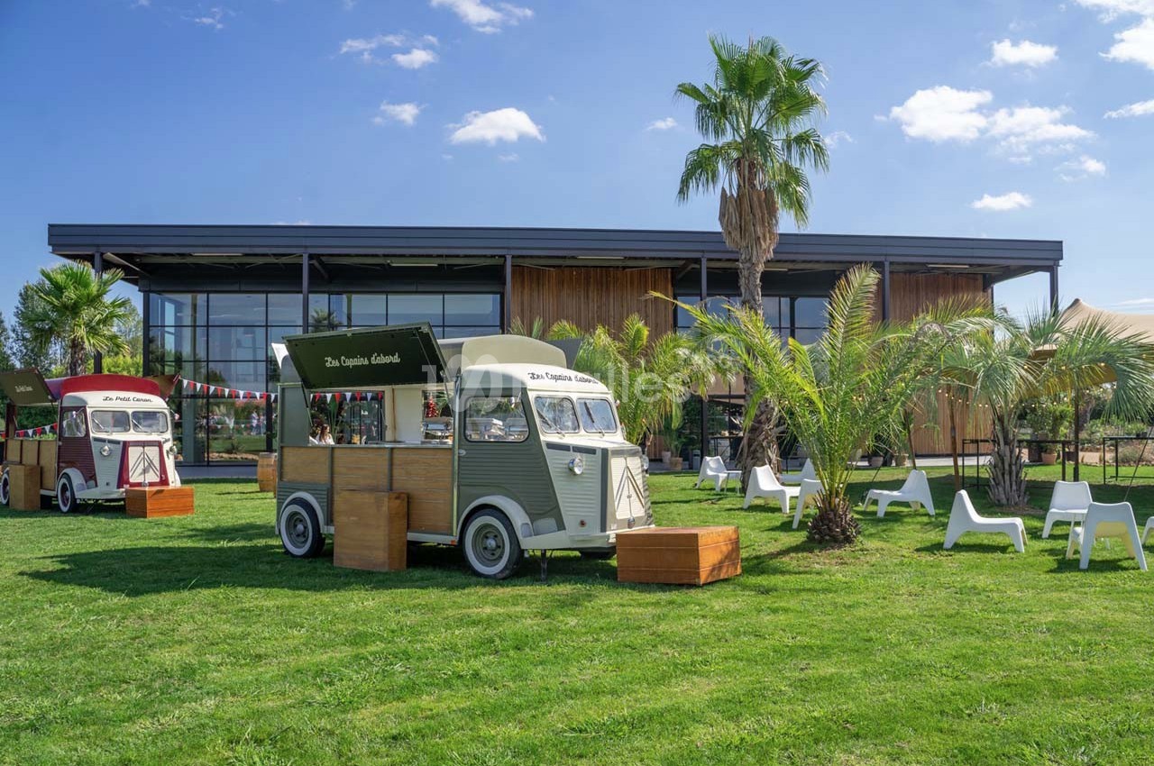 Deux food trucks vintage stationnés sur une pelouse, entourés de palmiers, devant un bâtiment moderne.