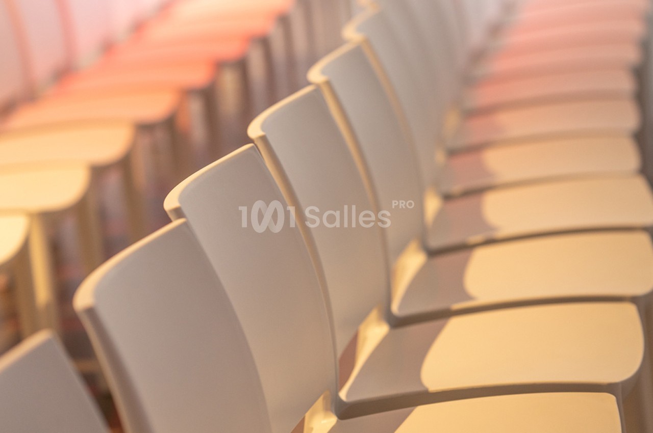 Rangée de chaises blanches alignées dans une salle éclairée par une lumière douce.