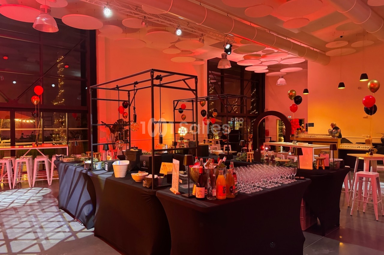 Salle décorée pour un événement avec tables, boissons, ballons rouges et noirs, éclairage tamisé.