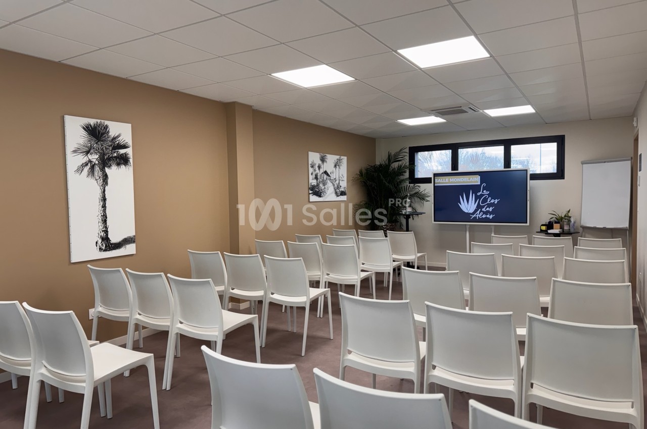 Salle de conférence lumineuse avec des chaises blanches alignées, un écran et des décorations murales.