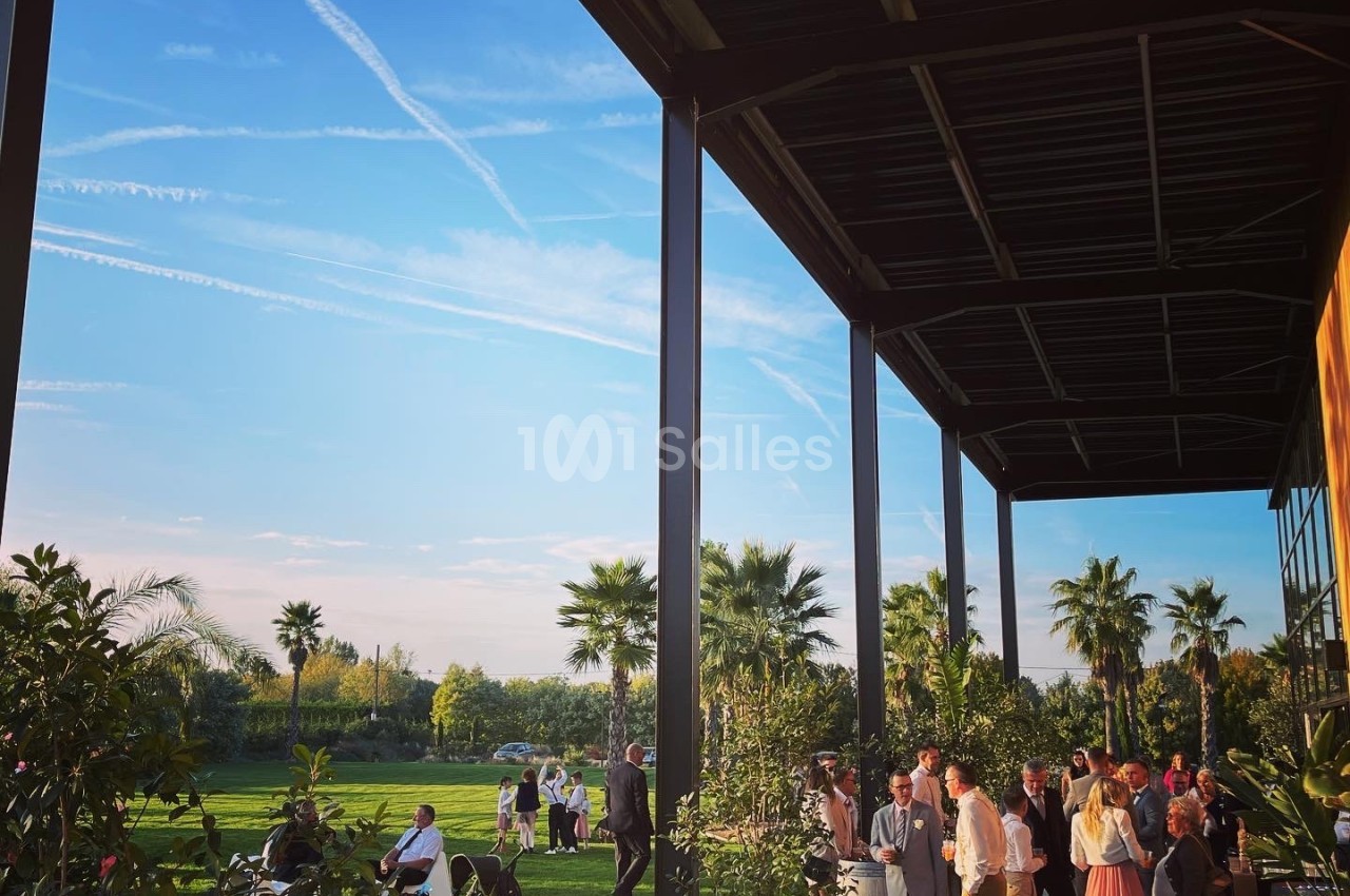 Groupe de personnes rassemblées sur une terrasse et une pelouse, entourées de végétation sous un ciel dégagé.