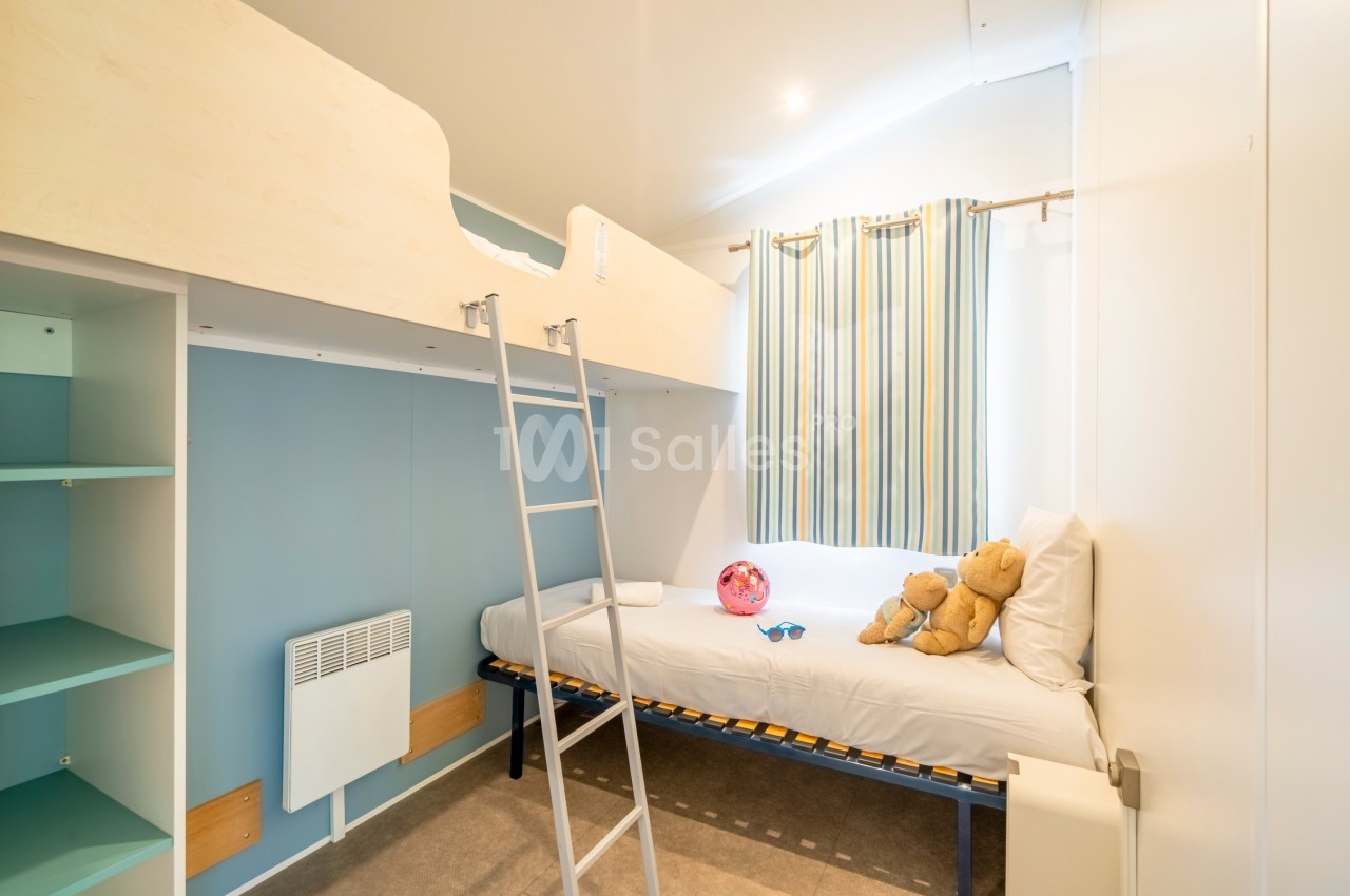 Chambre avec lits superposés, rideaux rayés, étagères ouvertes et jouets posés sur le lit inférieur.