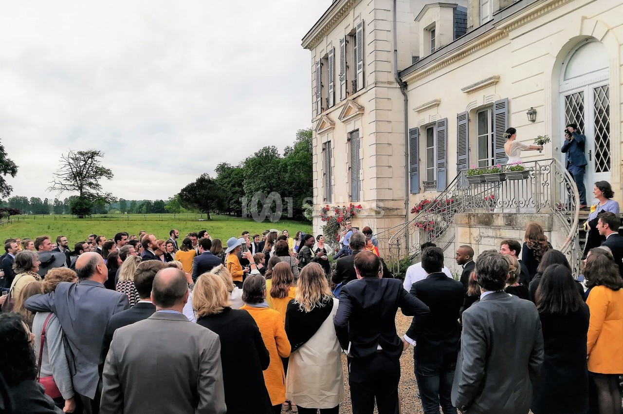 Groupe de personnes rassemblées devant un bâtiment ancien avec balcon, dans un cadre verdoyant.