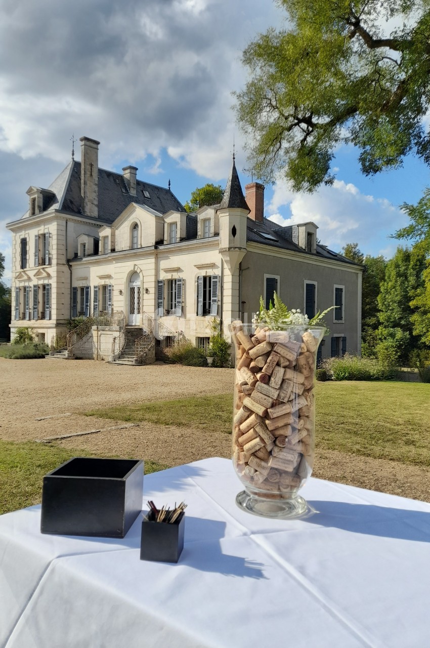 Un grand vase rempli de bouchons en liège posé sur une table blanche devant un château sous un ciel nuageux.