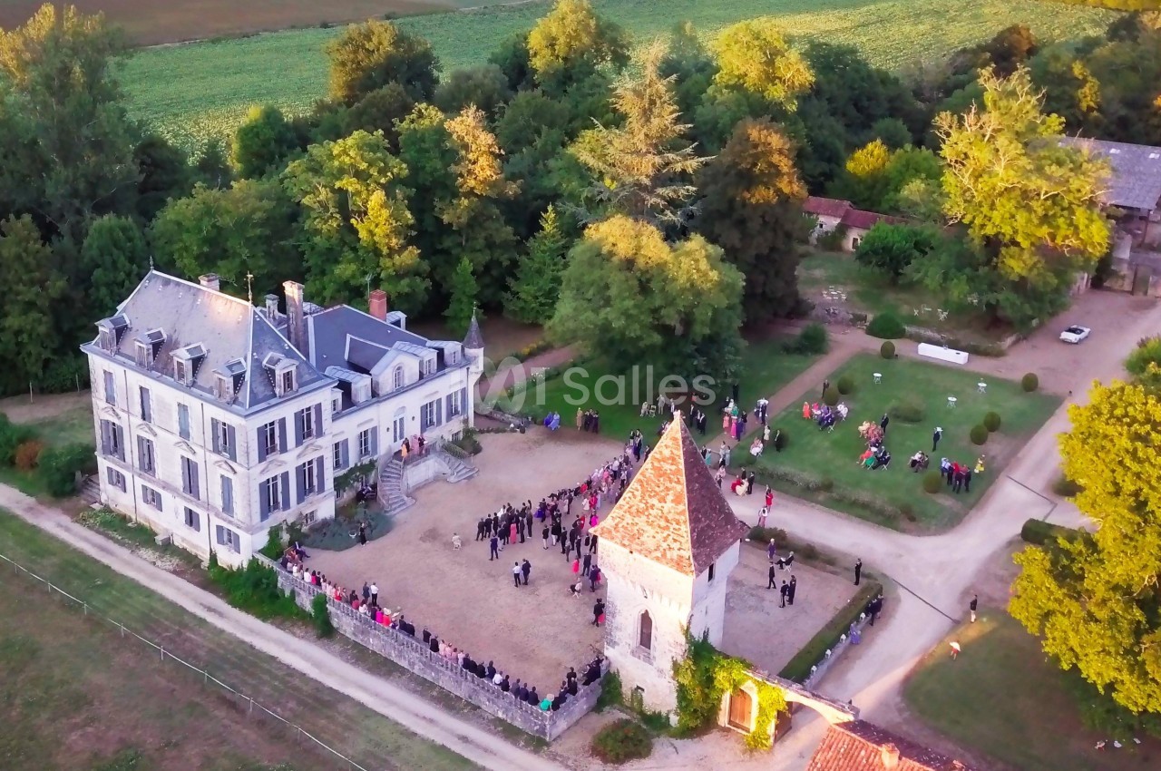 Vue aérienne d'un domaine avec une grande maison, une tour et des jardins, entouré de verdure et de visiteurs.