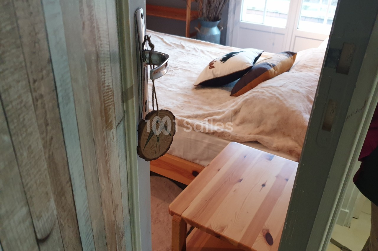 Vue d'une chambre avec un lit double, une table en bois et une fenêtre laissant entrer la lumière naturelle.
