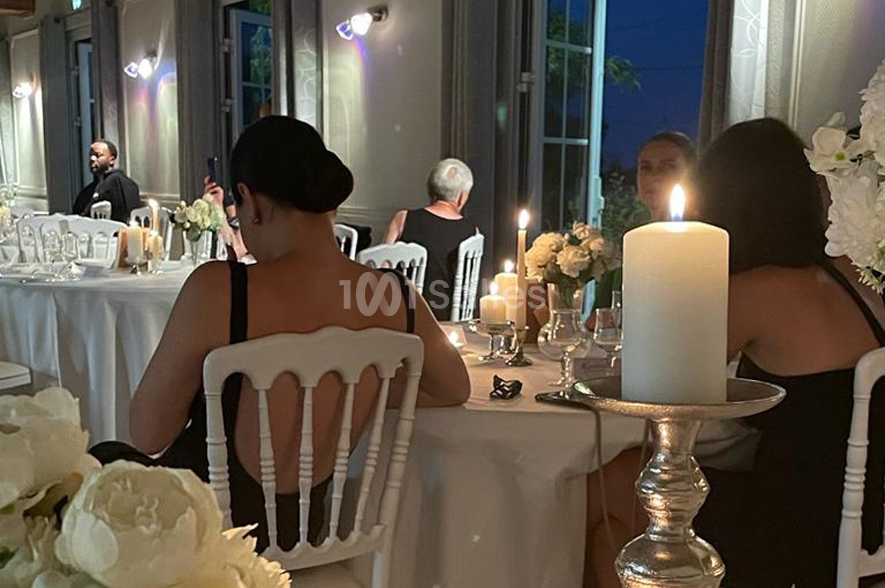Des invités assis autour de tables décorées de bougies et de fleurs blanches dans une salle de réception en soirée.