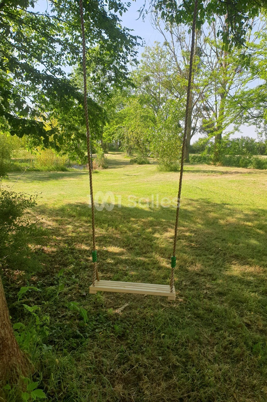 Balançoire en bois suspendue à des cordes, installée entre des arbres dans un jardin verdoyant.