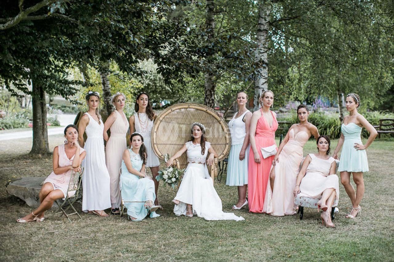 Une mariée en robe blanche entourée de demoiselles d'honneur en robes pastel dans un jardin verdoyant.
