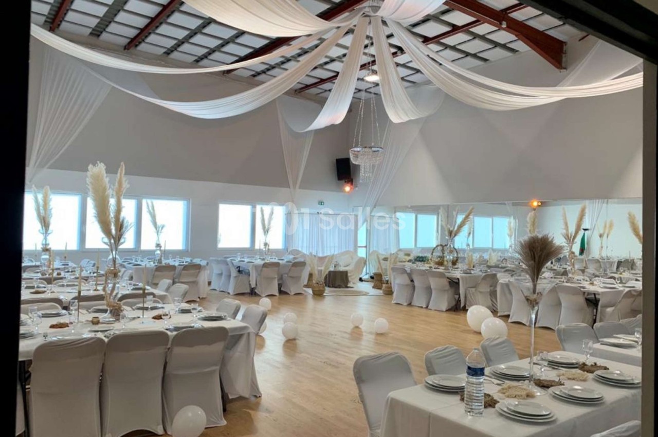 Salle de réception décorée avec des nappes blanches, des tables dressées et des drapés suspendus au plafond.