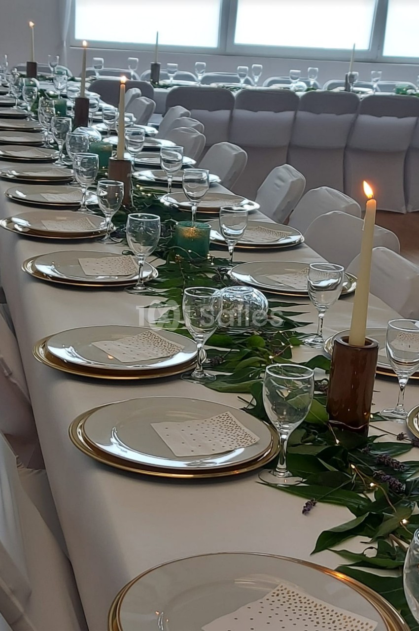 Table décorée pour un événement, avec vaisselle élégante, bougies allumées et feuillage en centre de table.