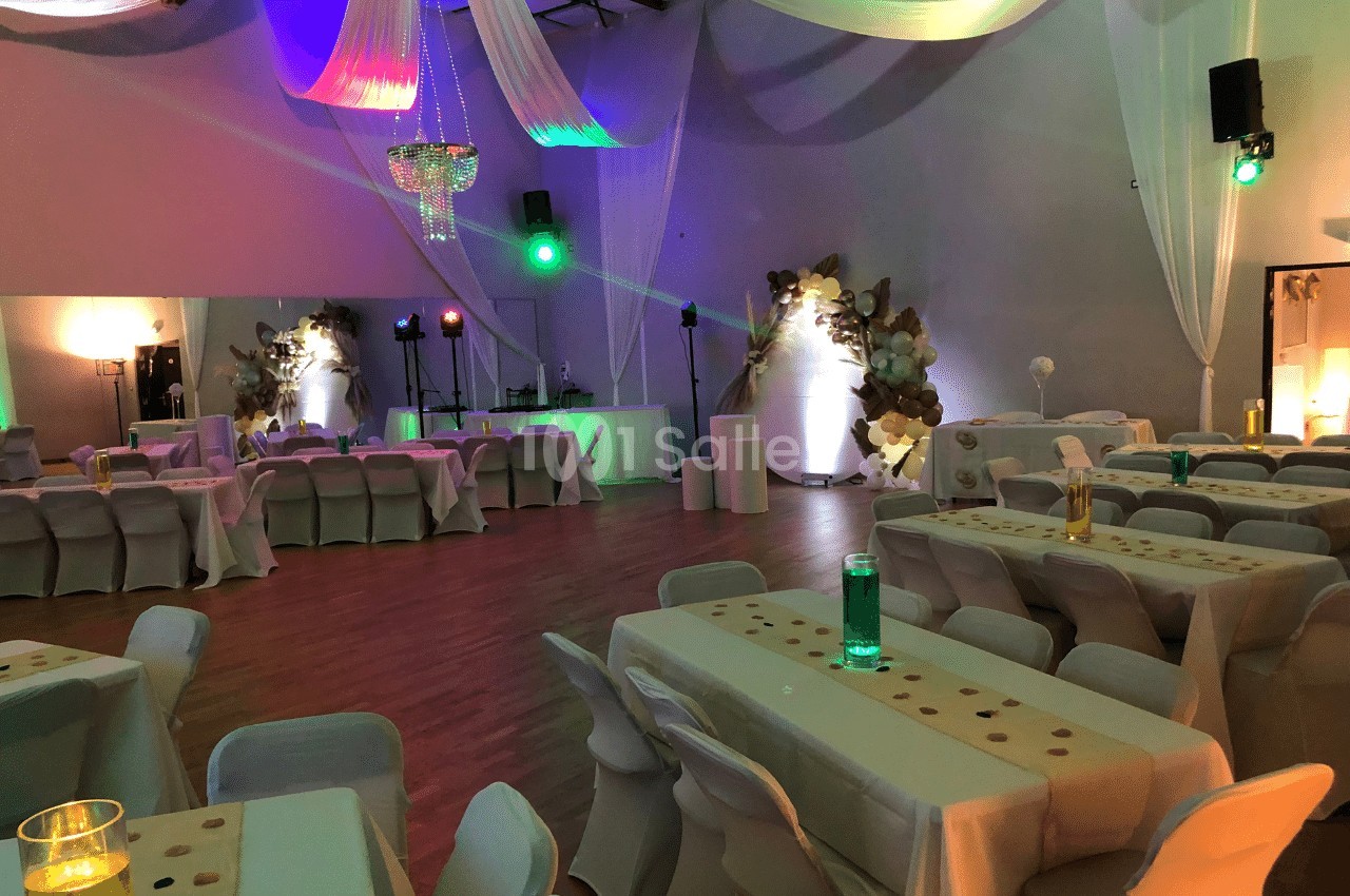 Salle de réception décorée avec des tables drapées, éclairages colorés et éléments suspendus.