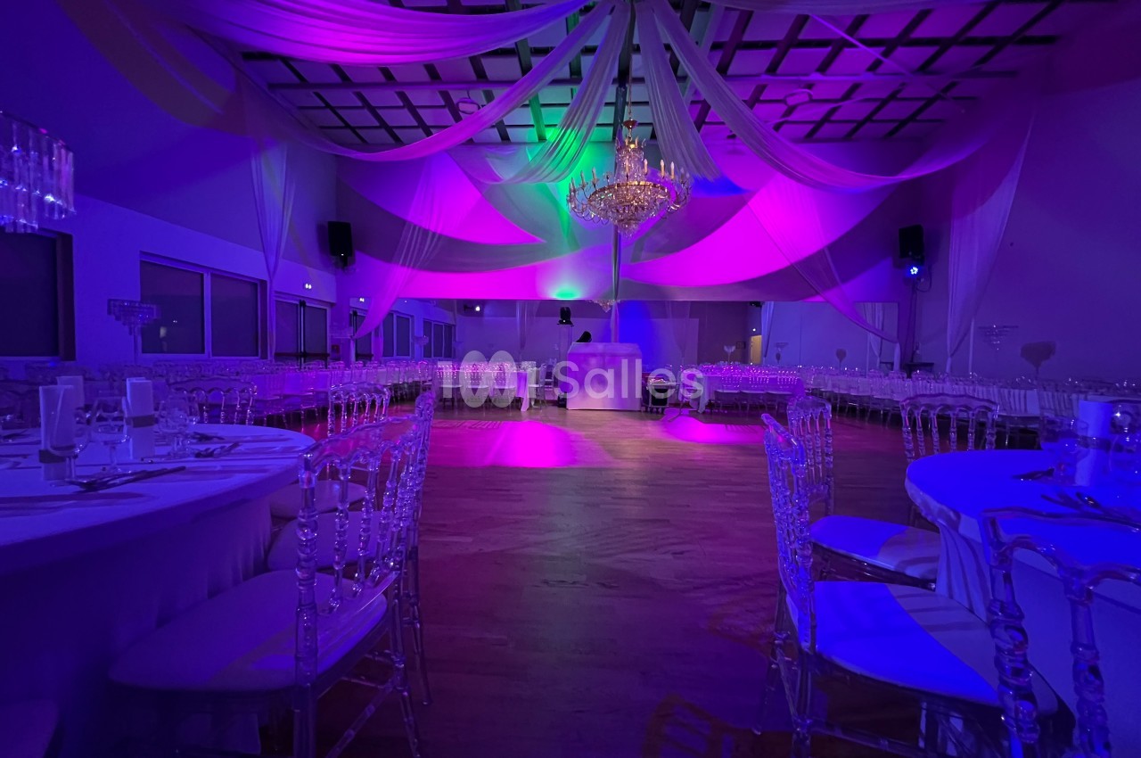 Salle de réception décorée avec des drapés suspendus, des chaises transparentes et un éclairage coloré.