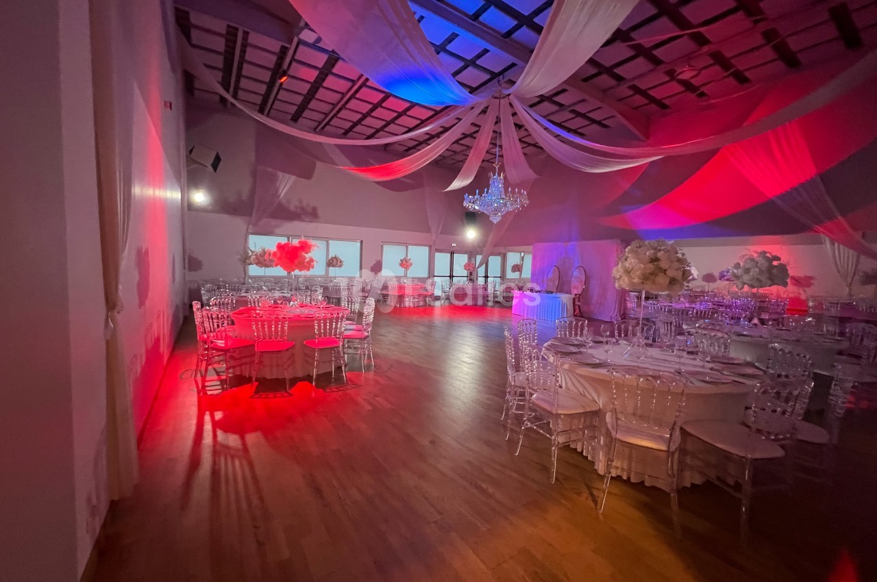 Salle de réception décorée avec des tables rondes, des chaises transparentes, un éclairage rouge et un lustre central.